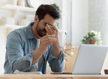 Man rubbing his eyes in distress while sitting at a computer